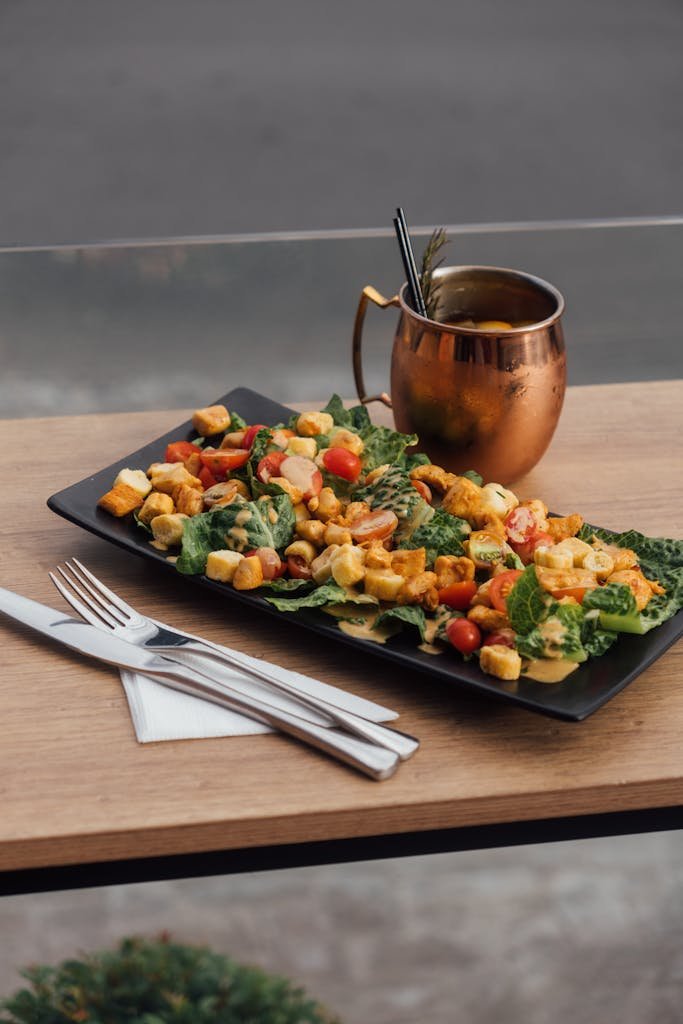 A fresh Caesar salad with croutons, cherry tomatoes, and a copper mug on wooden table.